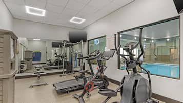 A fitness center with cardio machines, a pool, and a mirrored wall.