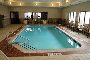 Una piscina interior con indicador de profundidad de 3 pies, sillas alrededor y señales de salida.
