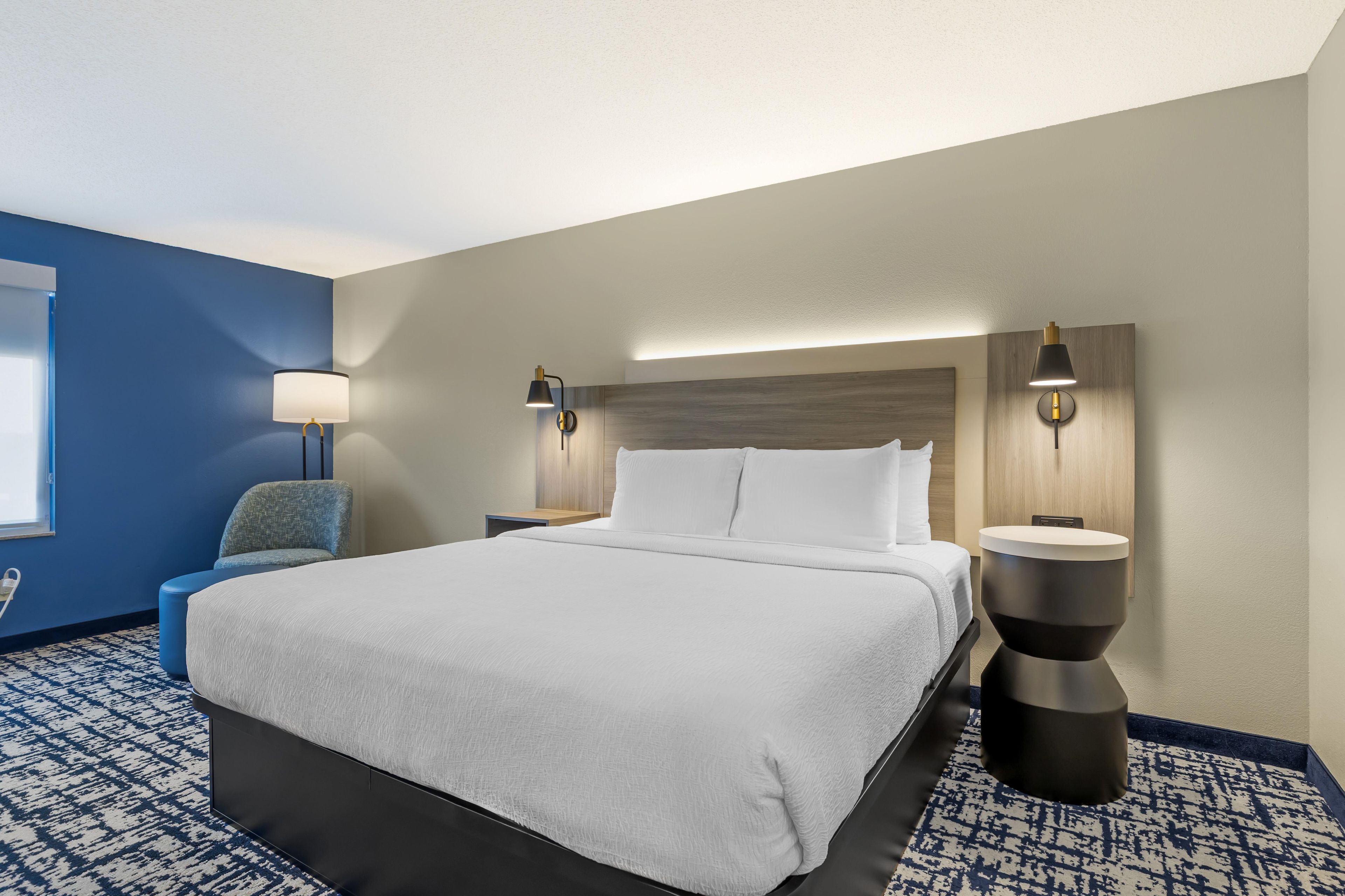A hotel room with a large bed, two bedside tables, a chair, and a wall-mounted lamp.