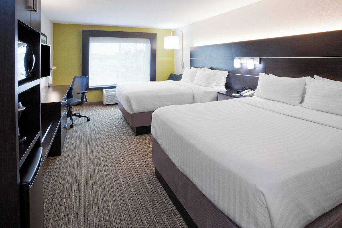 Une chambre d’hôtel avec deux lits, un bureau, une chaise, une télévision et une fenêtre.
