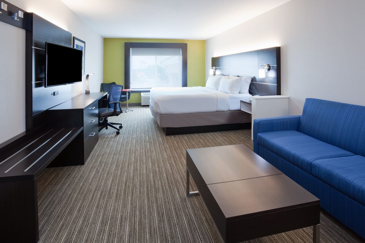Habitación de hotel con cama, escritorio con televisor de pantalla plana, sofá azul y una mesita pequeña.