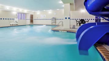 Una piscina interior con un tobogán azul, un elevador de piscina y un reloj en la pared.