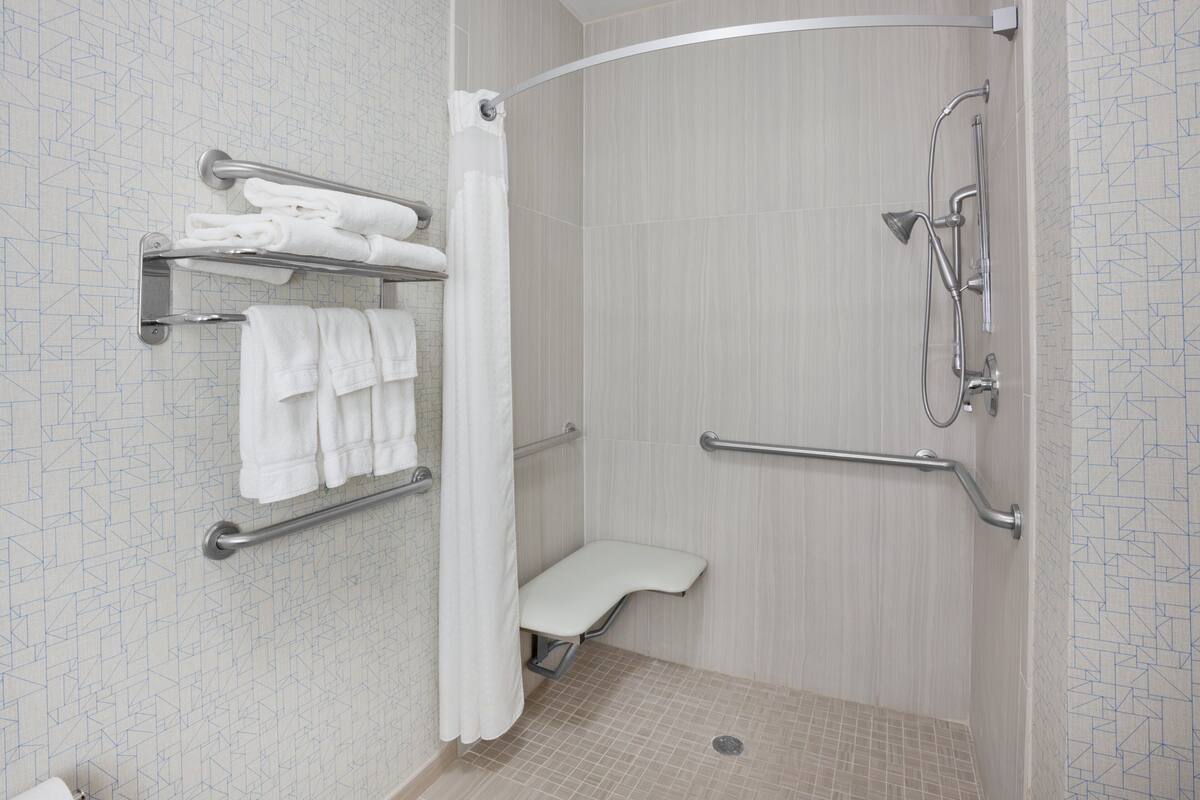 Zona de ducha con barra de apoyo, perchero y asiento de ducha.