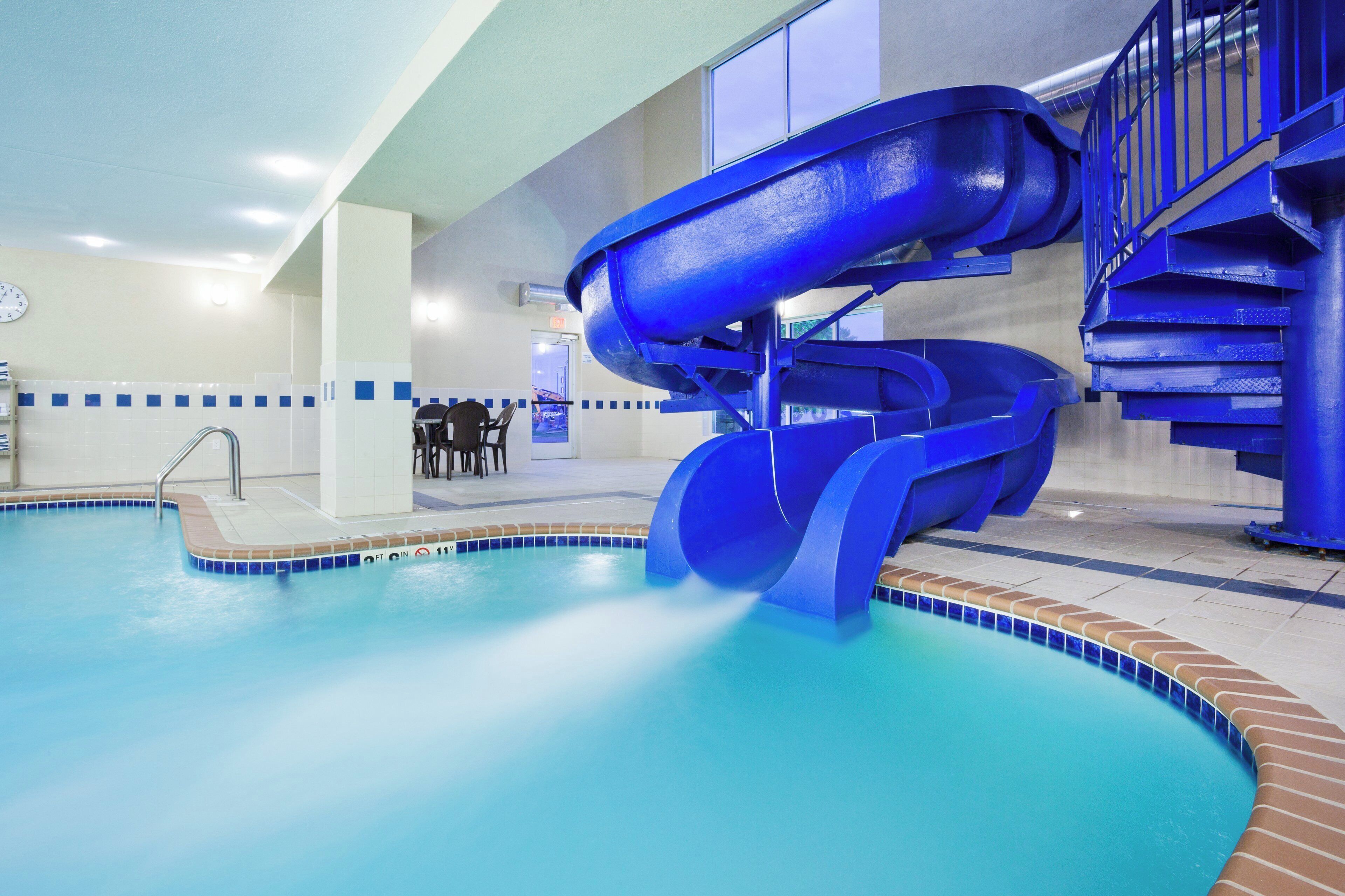 A swimming pool with a blue slide, a clock, and a seating area with tables and chairs.