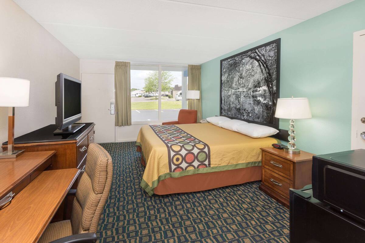 Une chambre d’hôtel équipée d’un lit, d’un bureau, d’une télévision, d’une commode et d’une fenêtre donnant sur l’extérieur.