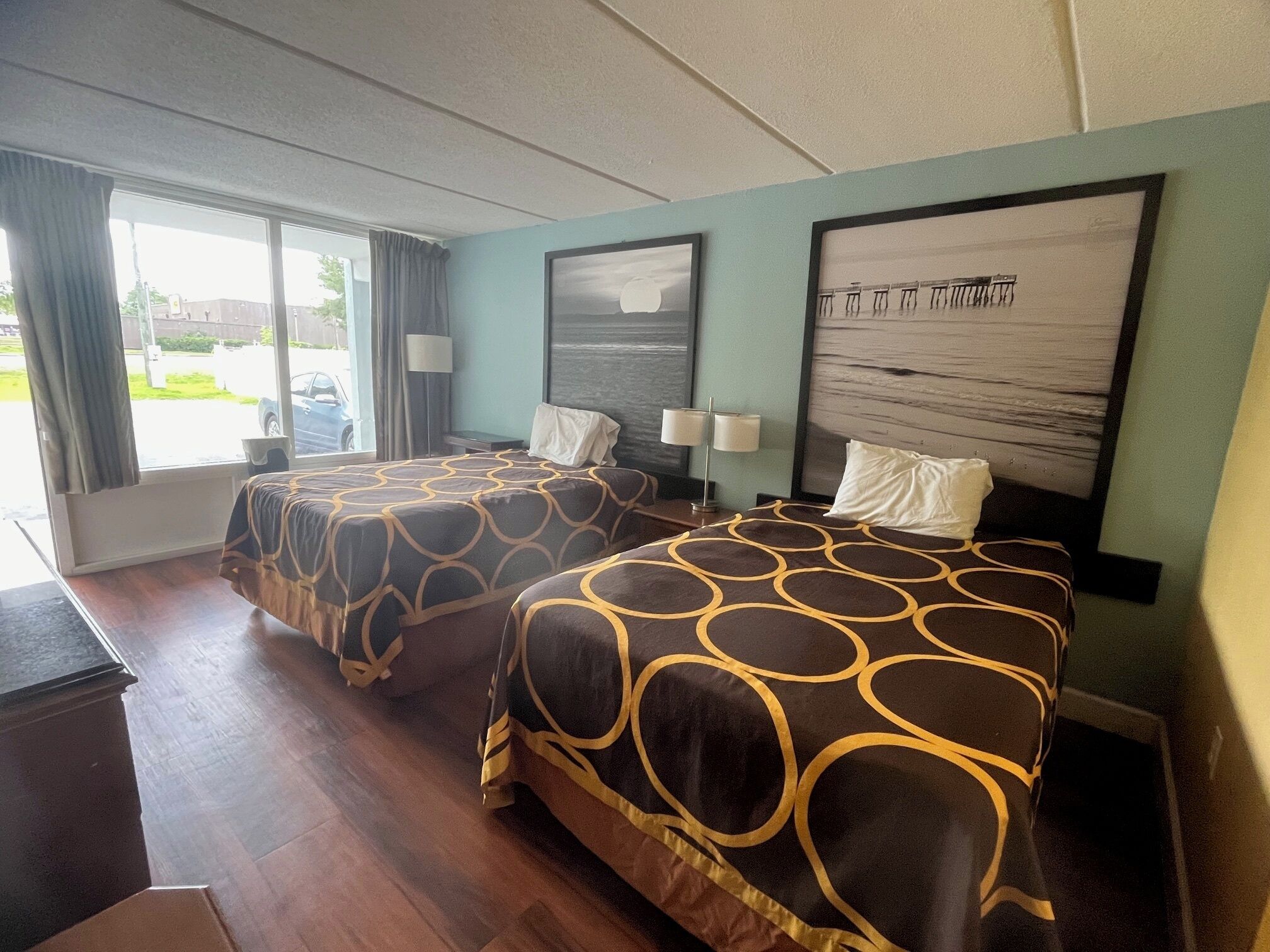A hotel room with two beds, a large window, and a view of the sea.