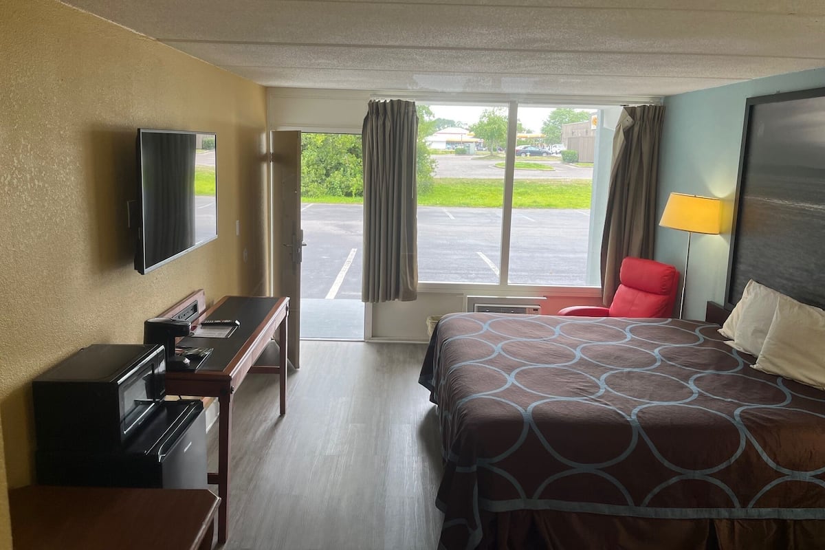 Une chambre d’hôtel équipée d’un lit, d’un bureau, d’une chaise, d’une télévision et offrant une vue sur le parking.