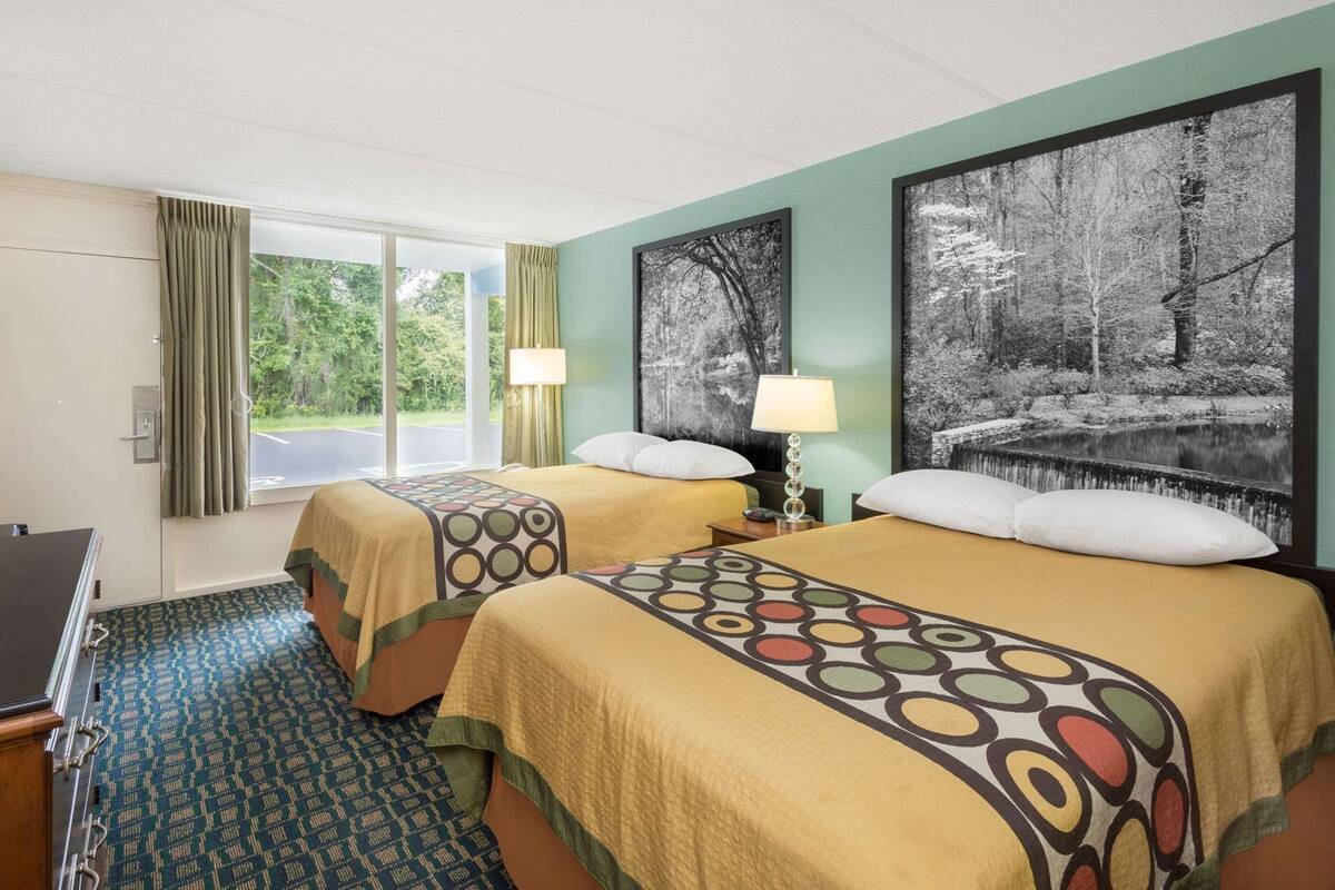 Une chambre d’hôtel avec deux lits, un bureau, une fenêtre avec des rideaux et deux lampes fixées au mur.