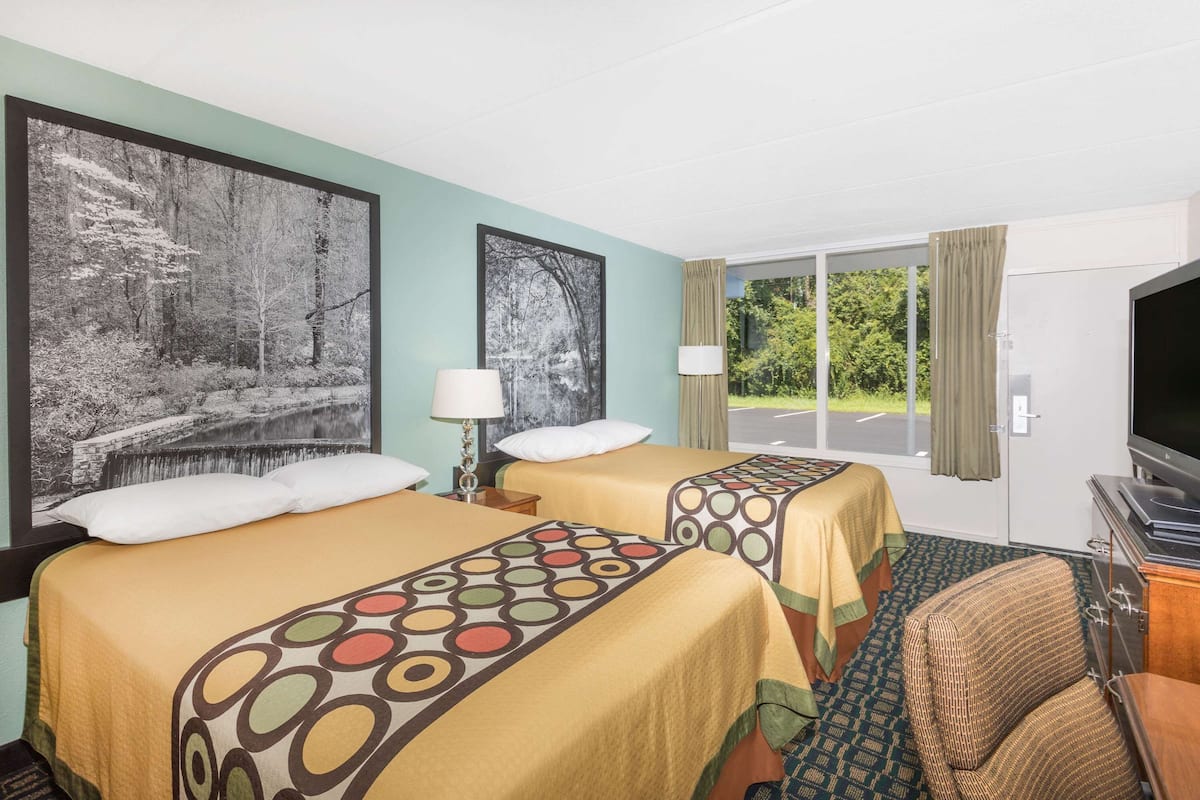 Une chambre d’hôtel avec deux lits, une télévision, une chaise et une grande fenêtre avec des rideaux.