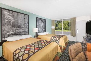 Habitación de hotel con dos camas, un televisor, una silla y un ventanal grande con cortinas.
