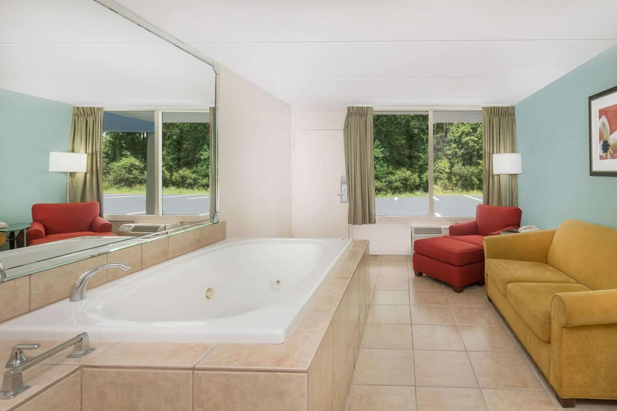 Une salle de bain moderne avec une grande baignoire, deux chaises rouges, un canapé jaune et un grand miroir.