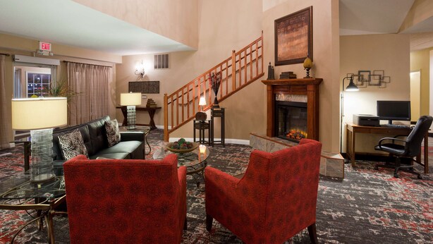 A living room with a fireplace, a staircase, and a desk with a computer. - GrandStay Residential Suites - Eau Claire (Eau Claire)