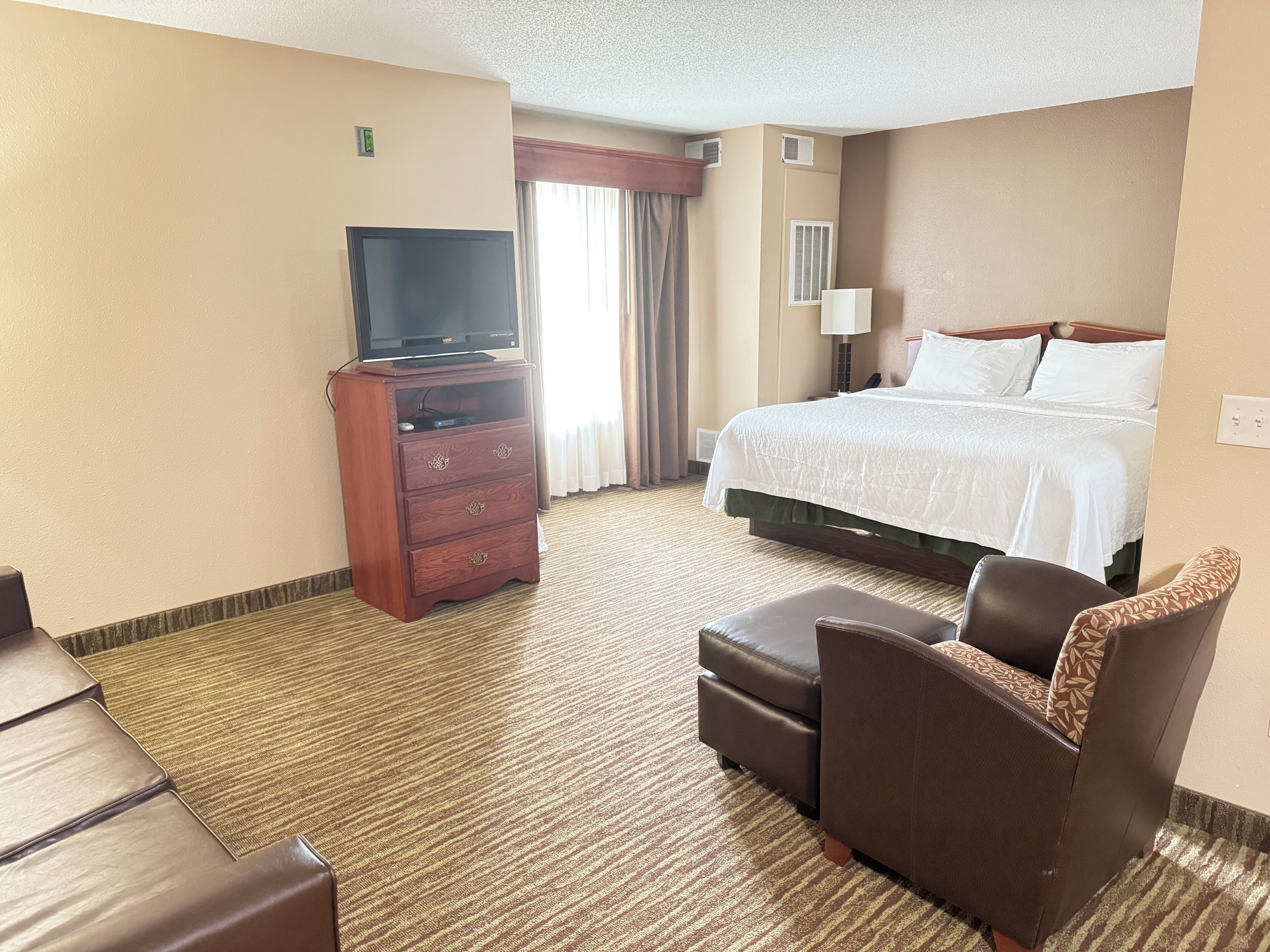 Ein Hotelzimmer mit einem Bett, einem Fernseher auf einer Holzkommode, einem Schreibtisch und einem Sessel.