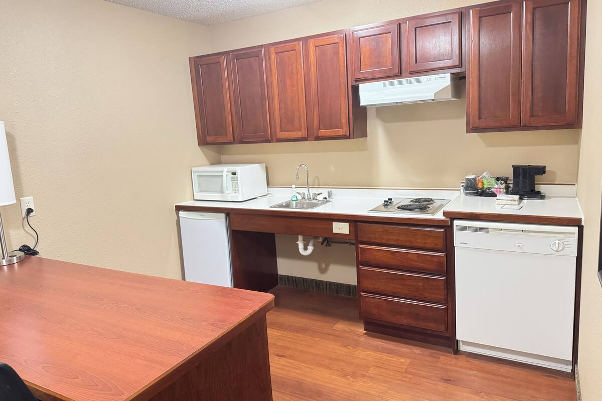 Una cocina compacta con armarios de madera, un microondas, un fregadero, un lavavajillas y una estufa.