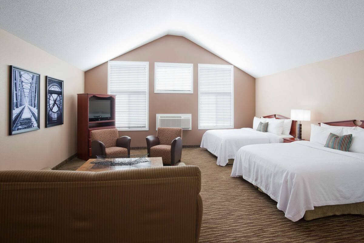 Habitación de hotel con dos camas, un televisor, un sofá y una mesa de comedor.