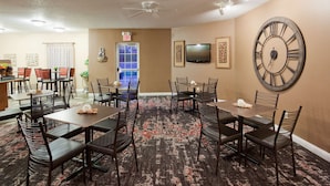 A dining area with multiple tables and chairs, a large wall clock, and a television mounted on the wall. - GrandStay Residential Suites - Eau Claire (Eau Claire)
