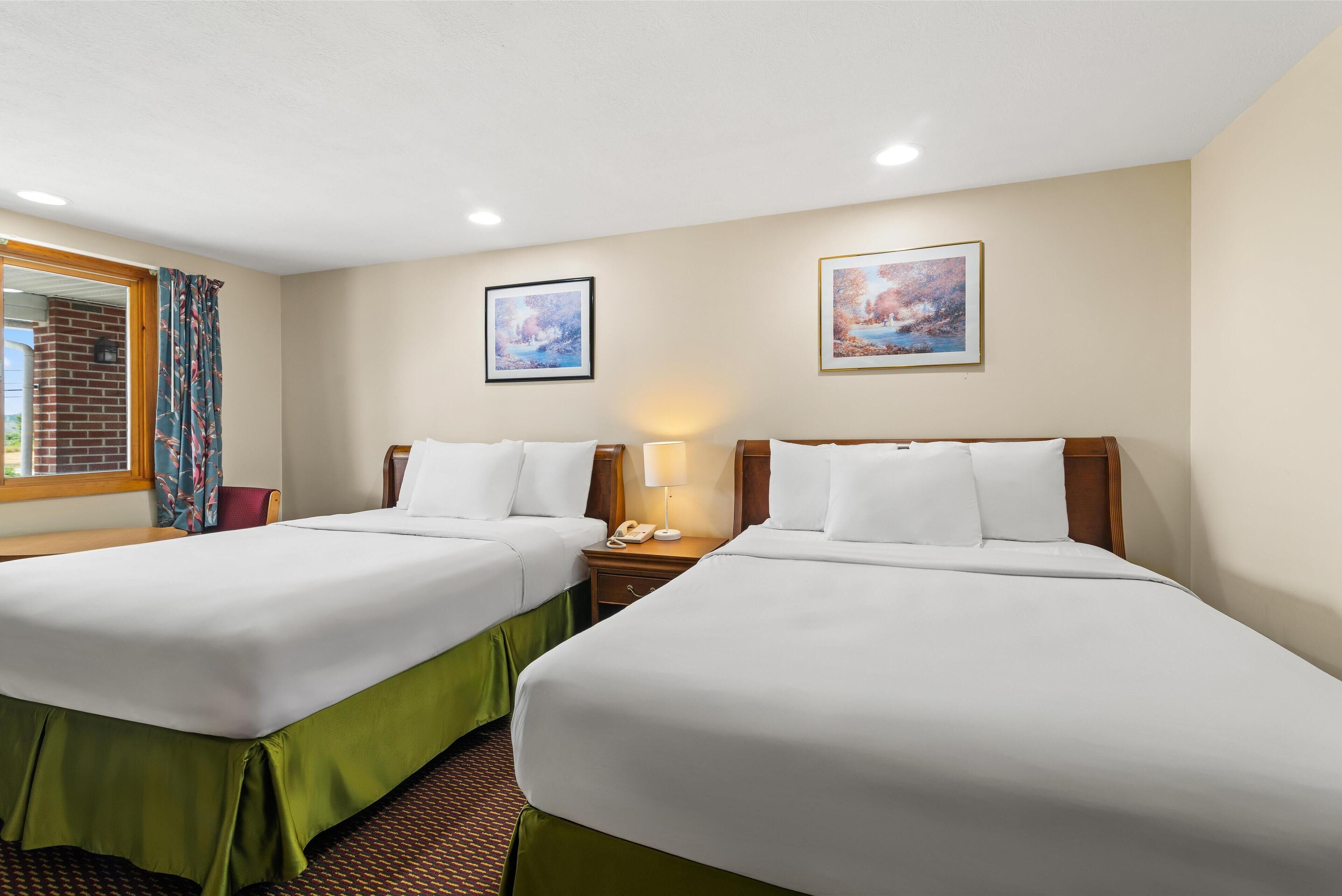 A hotel room with two beds, a window with curtains, a brick wall, and two framed pictures on the wall.
