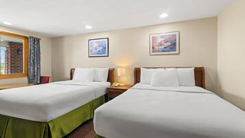 A hotel room with two beds, a window with curtains, a brick wall, and two framed pictures on the wall.