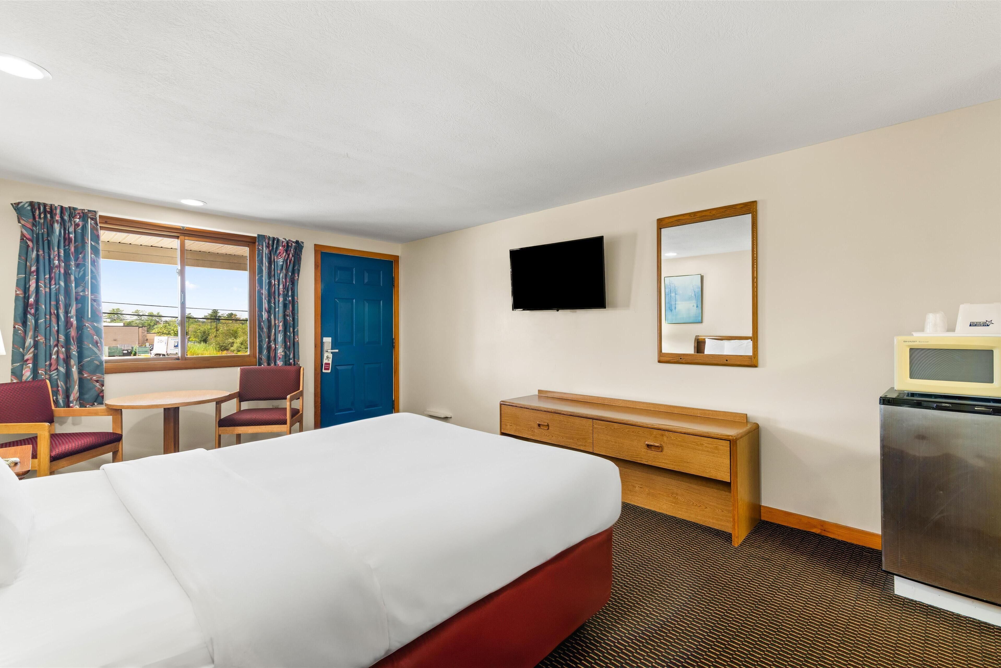 Een hotelkamer met een bed, een bureau, een stoel, een televisie, een spiegel en een koelkast.