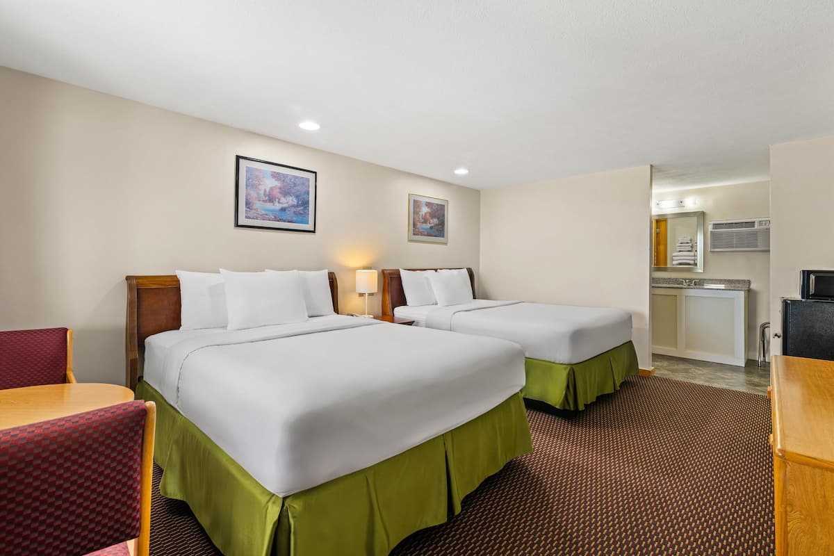 A hotel room with two beds, a desk, a chair, and a kitchenette.