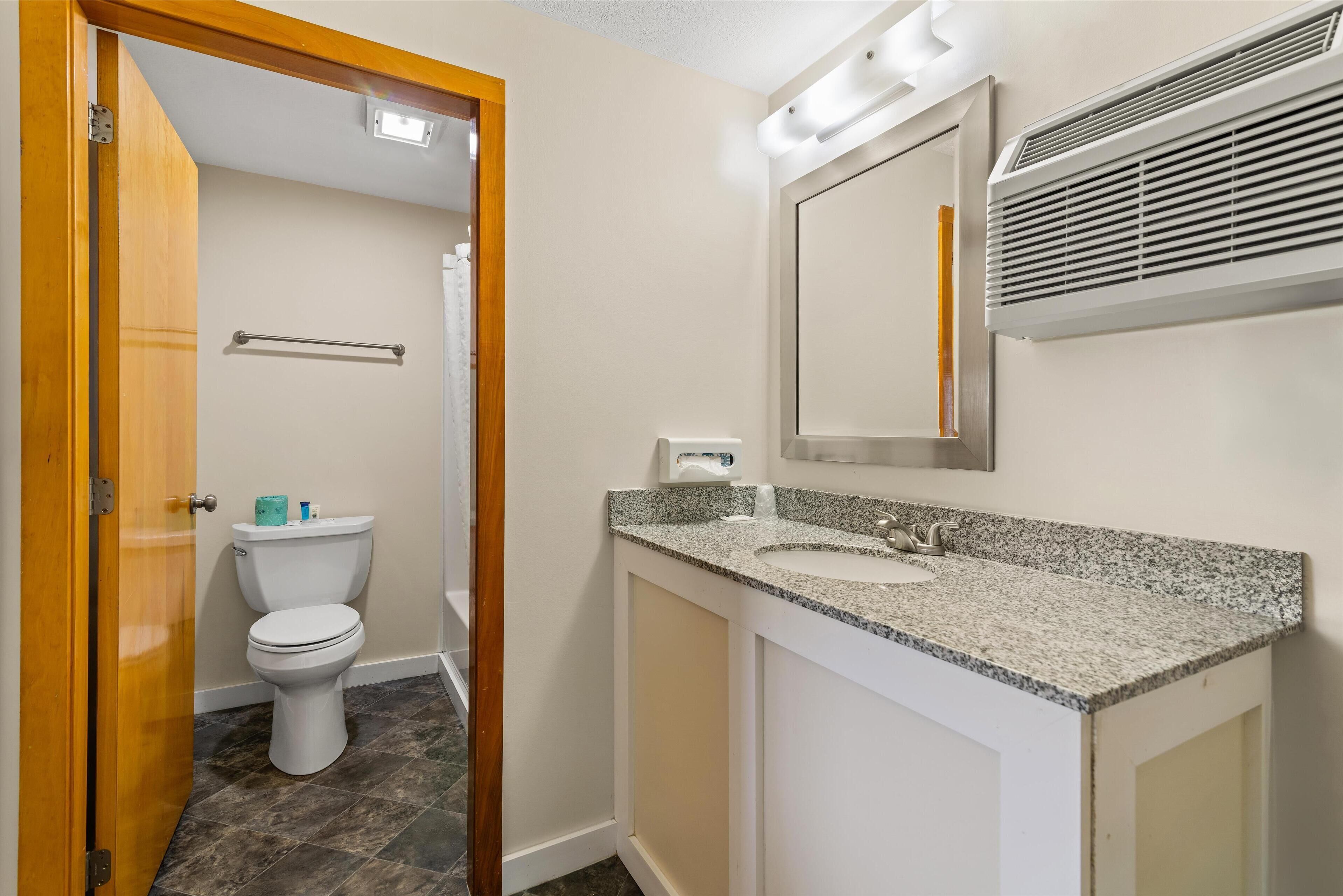 A bathroom with a toilet, sink, mirror, and shower.