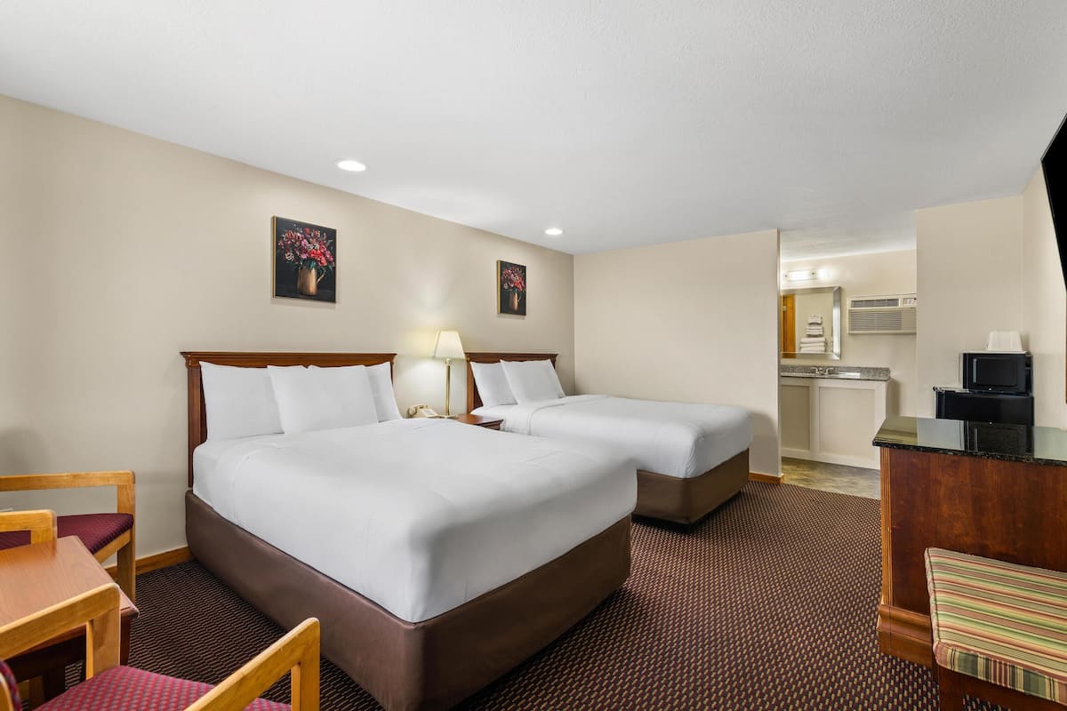 A hotel room with two beds, a desk, a chair, a TV, and a kitchenette.