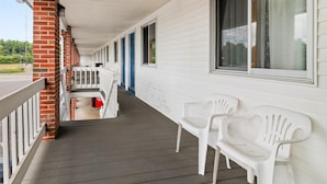 A covered porch with white plastic chairs, a brick wall, and a row of windows. - Americas Best Value Inn Biddeford Portland (Biddeford)