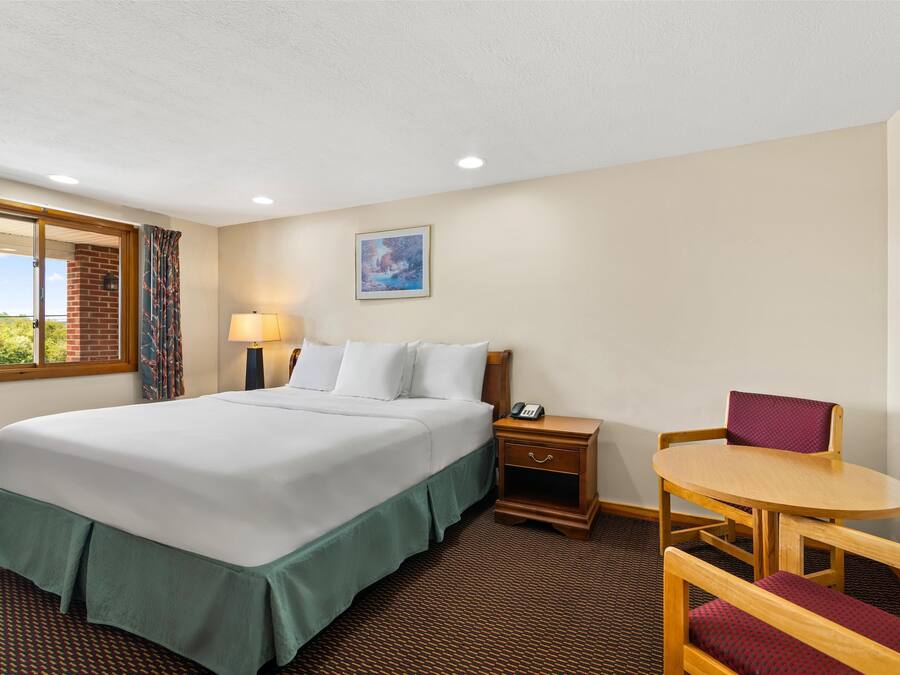 Une chambre d’hôtel équipée d’un lit, d’un bureau, d’une chaise, d’une table de chevet, d’une lampe et d’une fenêtre donnant sur un paysage verdoyant.