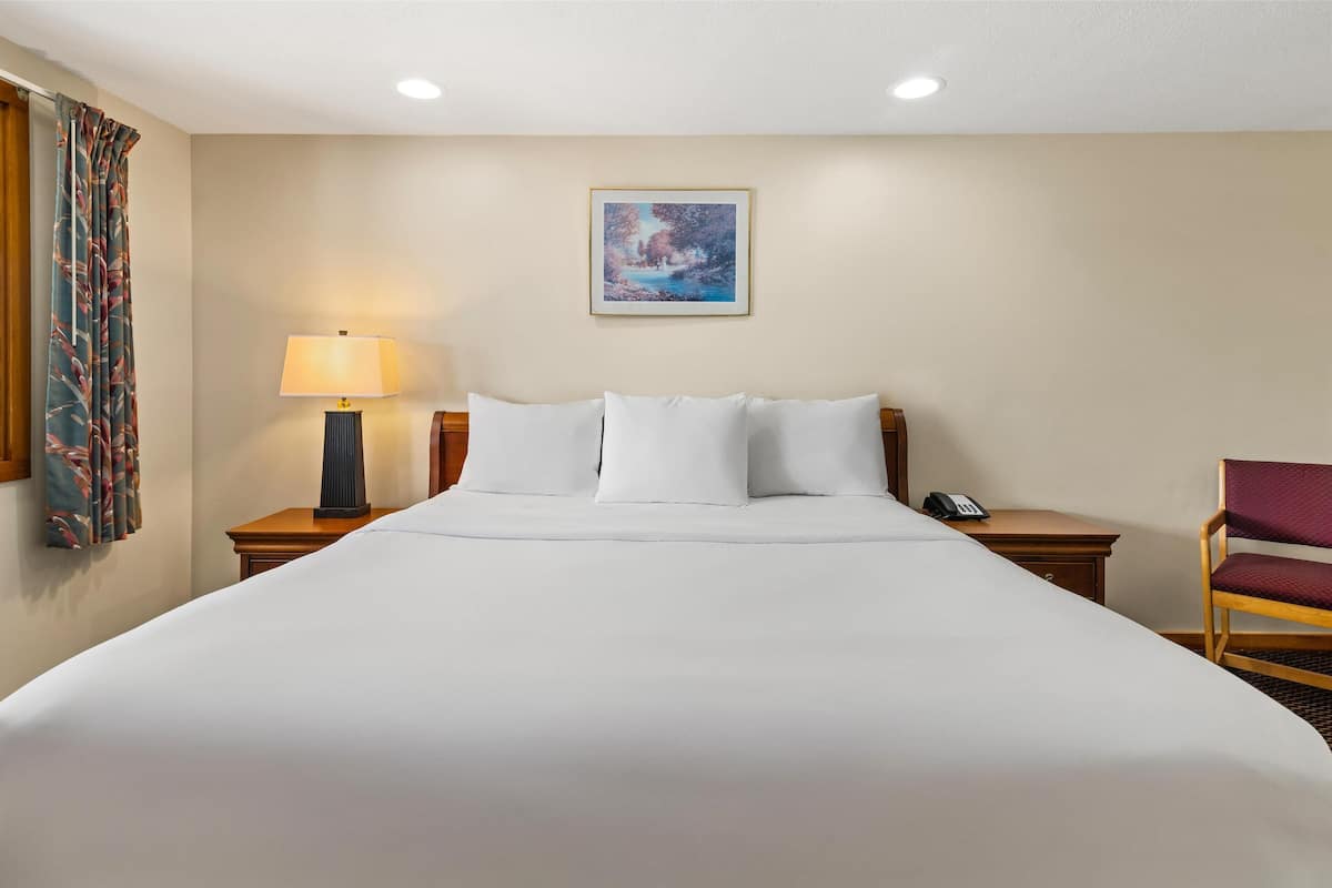 A neatly made bed with white linens, a bedside lamp, a telephone, and a chair.
