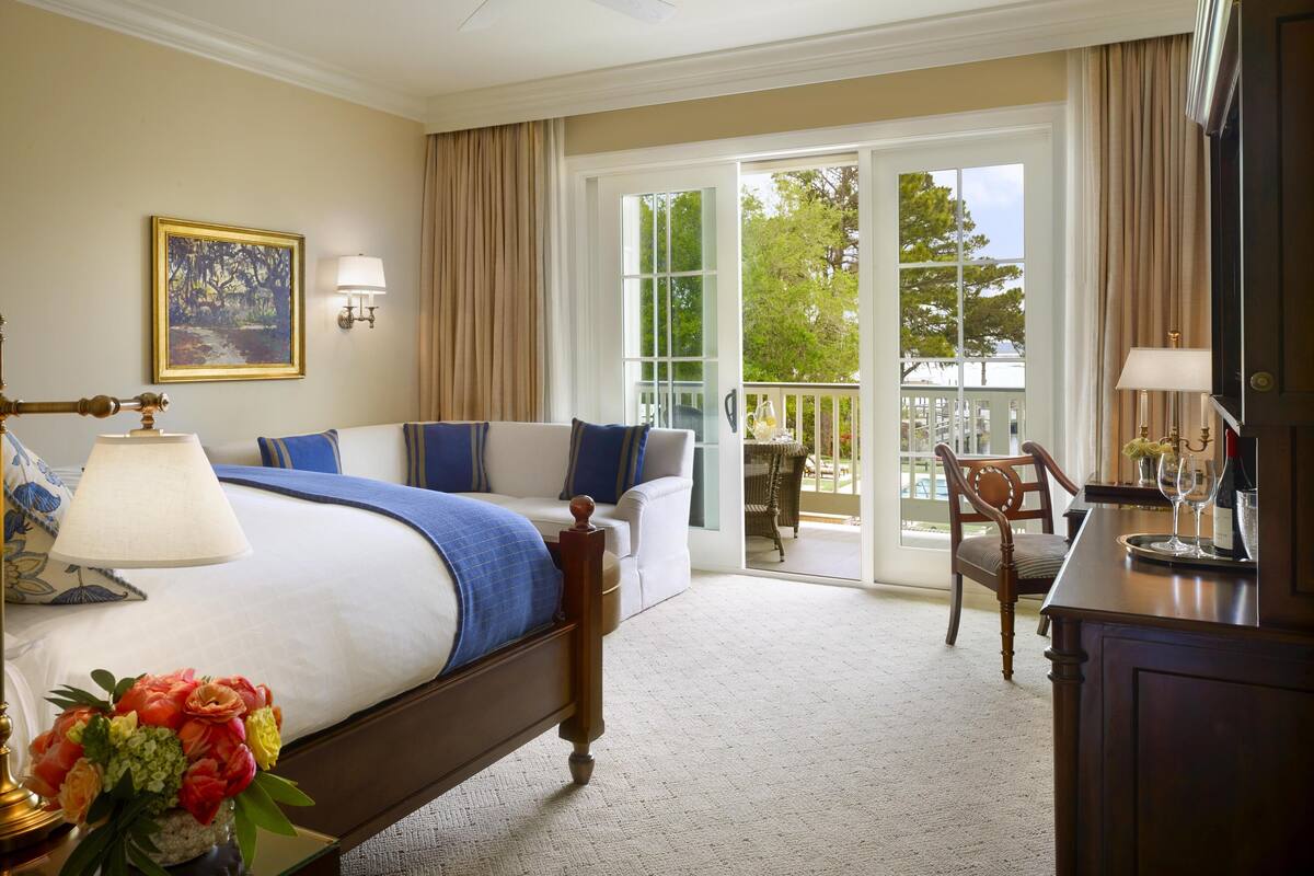 Ein Hotelzimmer mit Bett, Schreibtisch, Stuhl, Balkon mit Tisch und Deckenventilator.