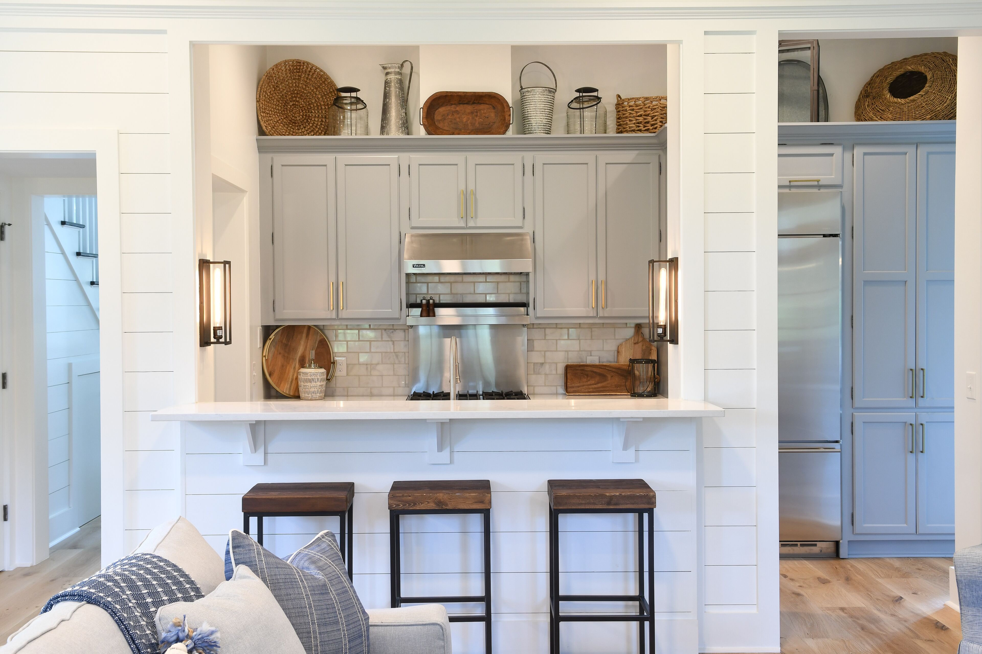 Una cocina con armarios blancos, una campana extractora de acero inoxidable y una zona de bar con taburetes.