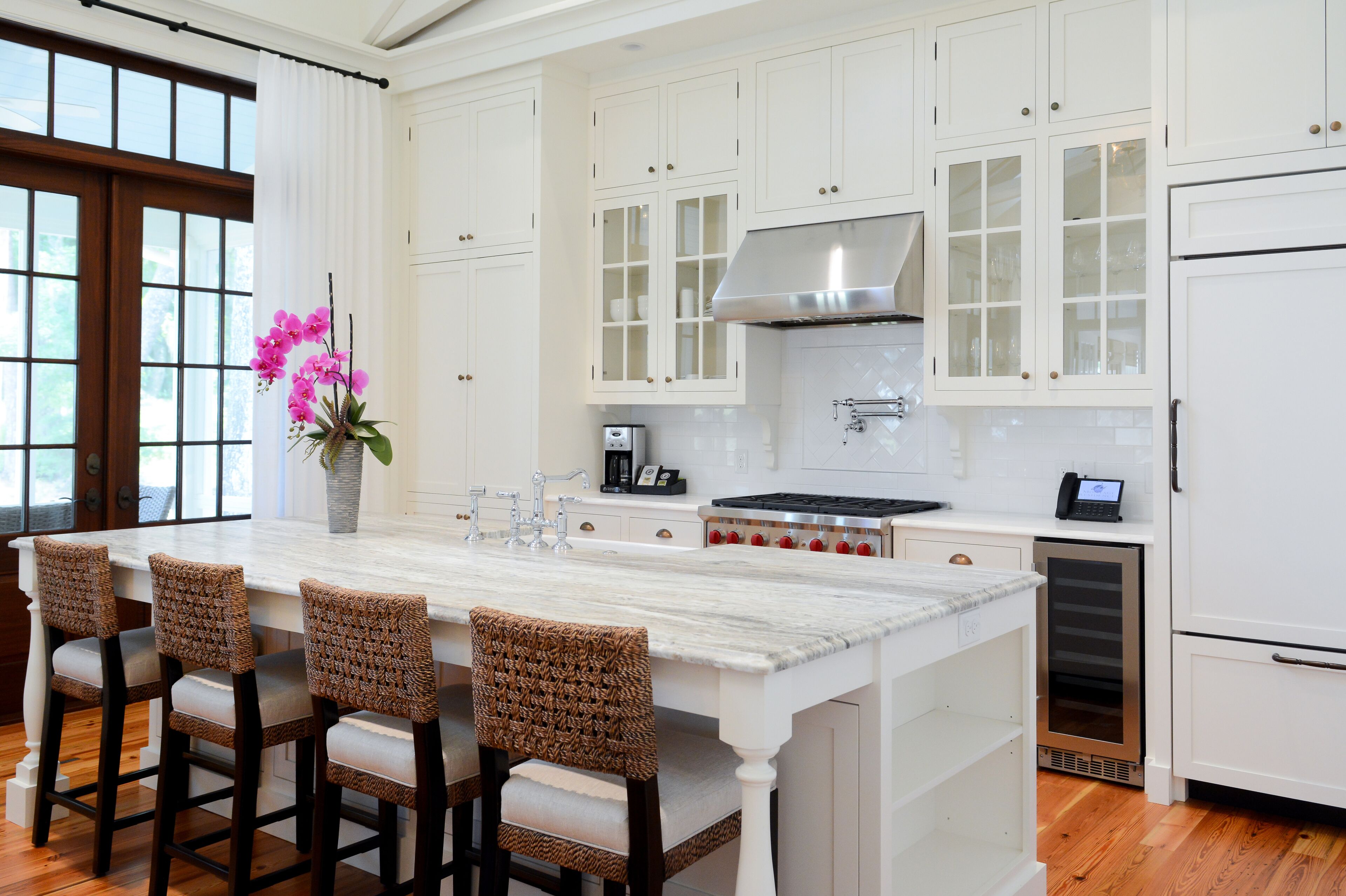 Una cocina moderna con armarios blancos, una isla grande con taburetes de bar, un extractor de acero inoxidable y un horno empotrado.