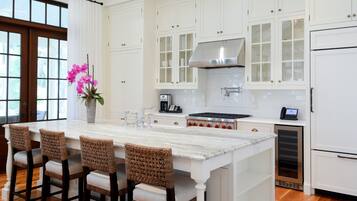 Una cocina moderna con armarios blancos, una isla grande con taburetes de bar, un extractor de acero inoxidable y un horno empotrado.