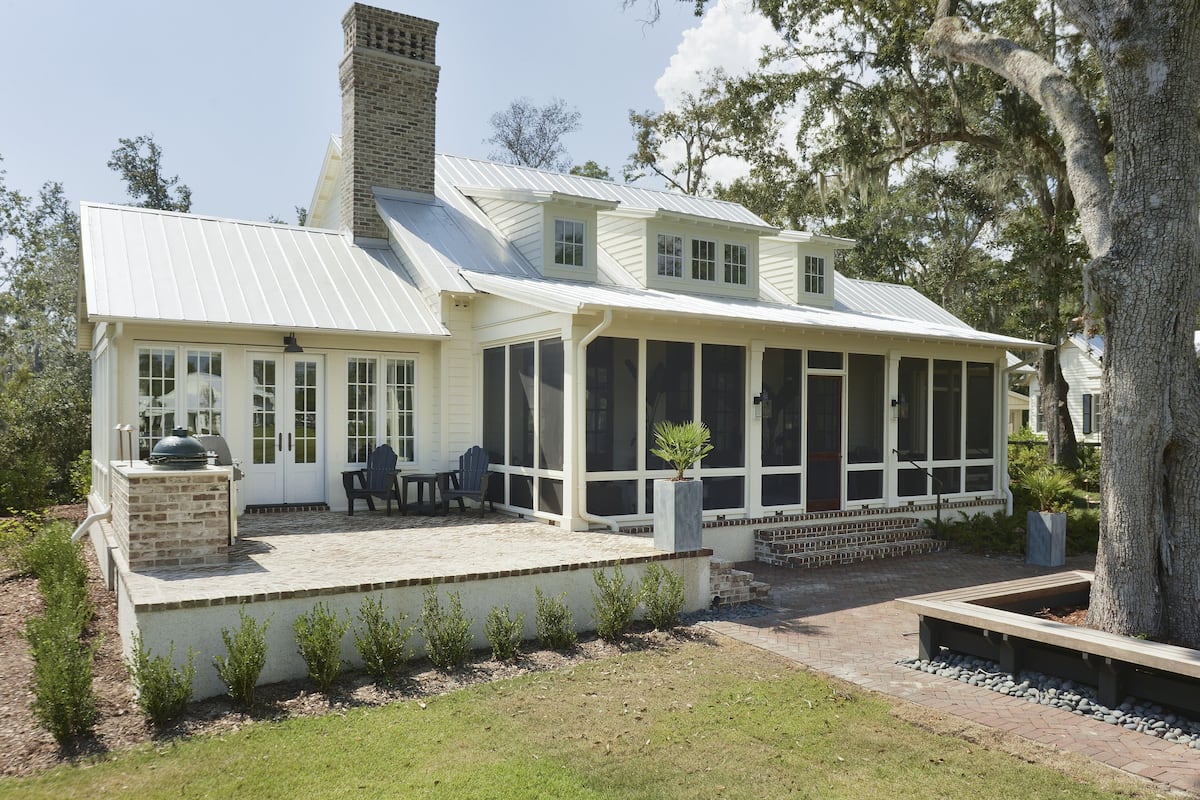 Ein Haus mit überdachter Terrasse, einem Backsteinsschornstein und einem kleinen Garten.