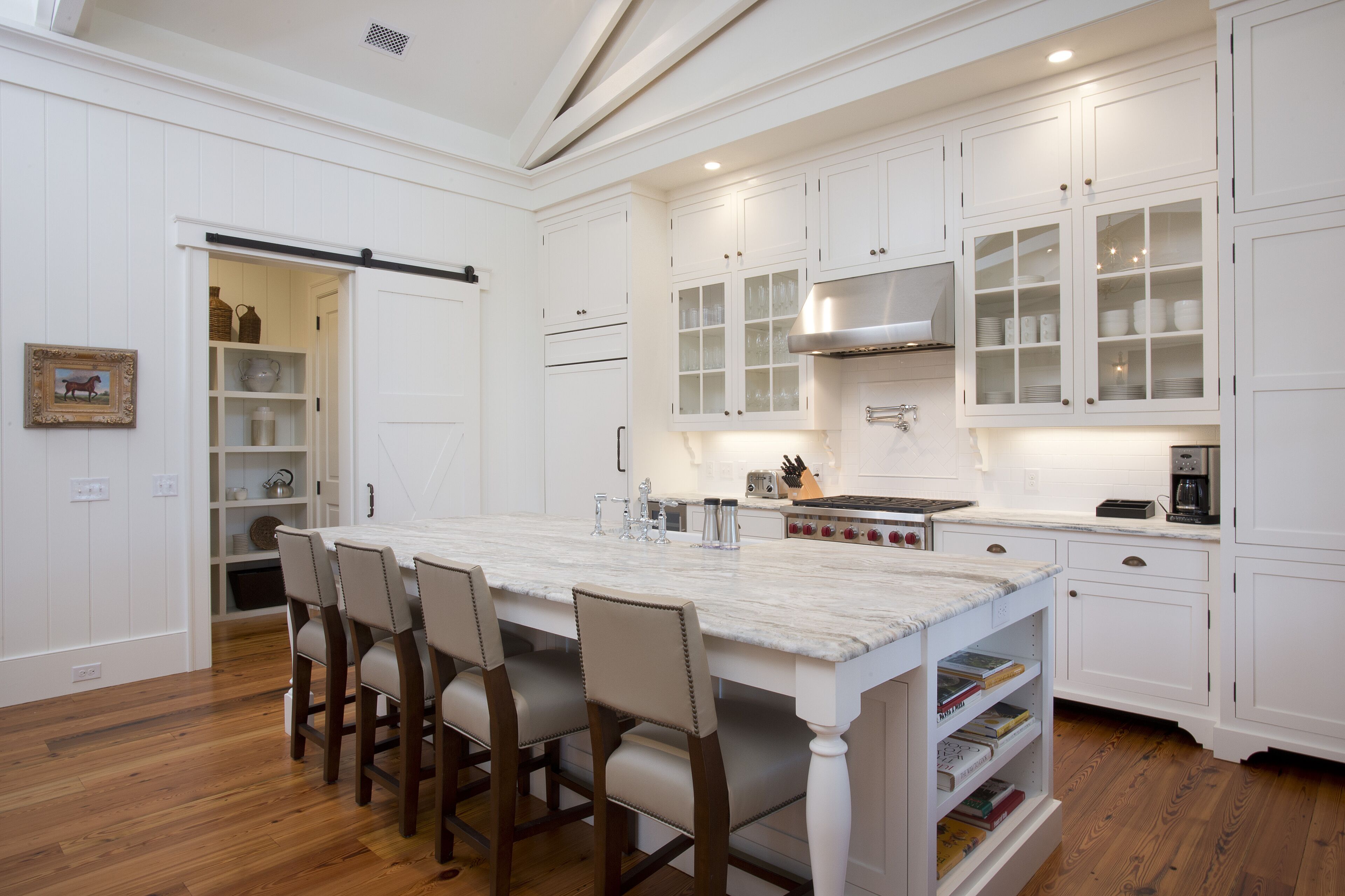 A spacious kitchen with white cabinetry, a marble island, and wooden chairs.