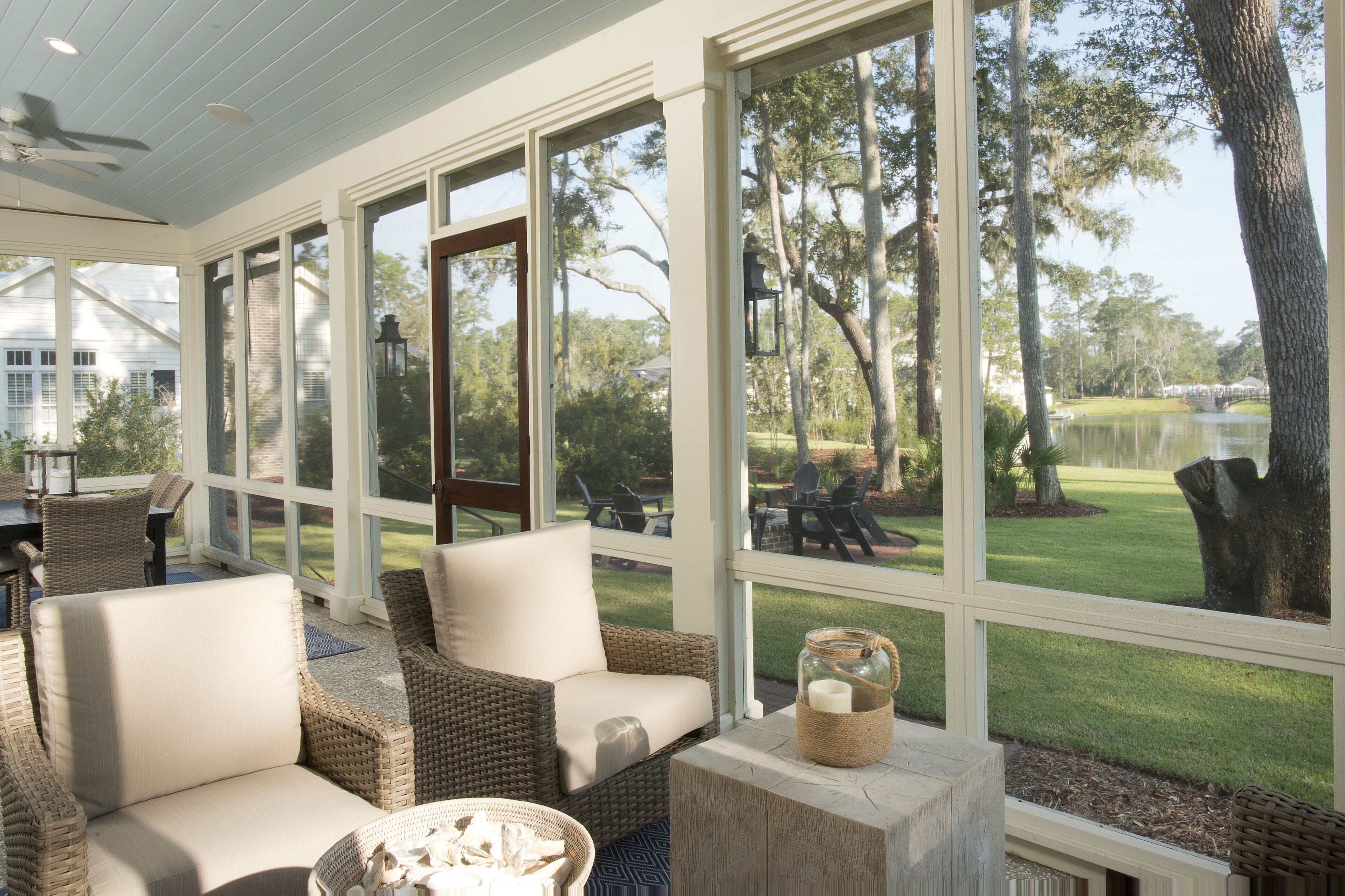 A covered patio with wicker furniture, large windows, and a view of a golf course.
