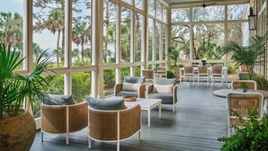 Un espacio al aire libre con techo, mobiliario de mimbre y amplias ventanas con vistas a un jardín.