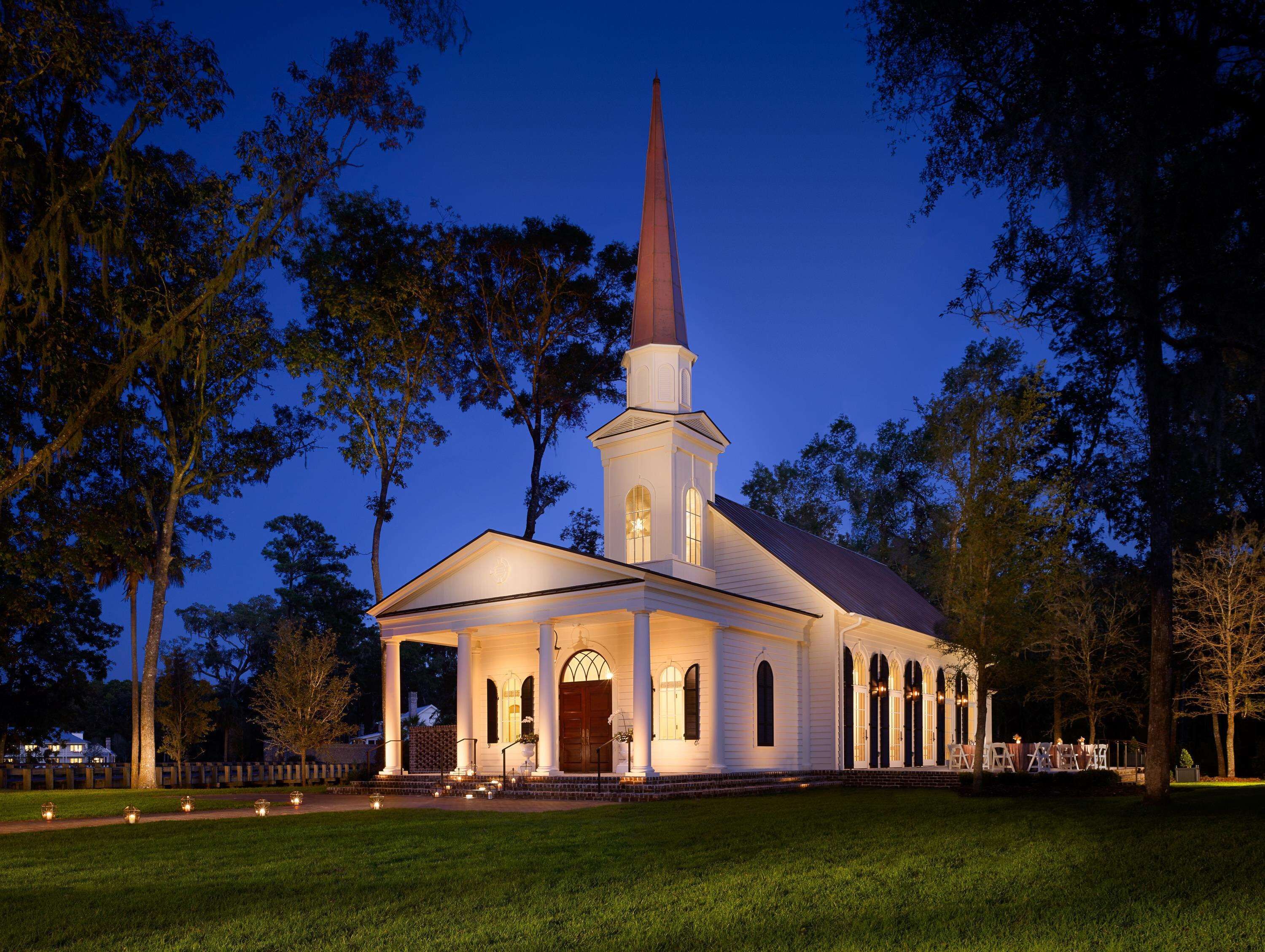 Une église blanche, dotée d’un clocher imposant, entourée d’arbres et d’une pelouse bien entretenue.