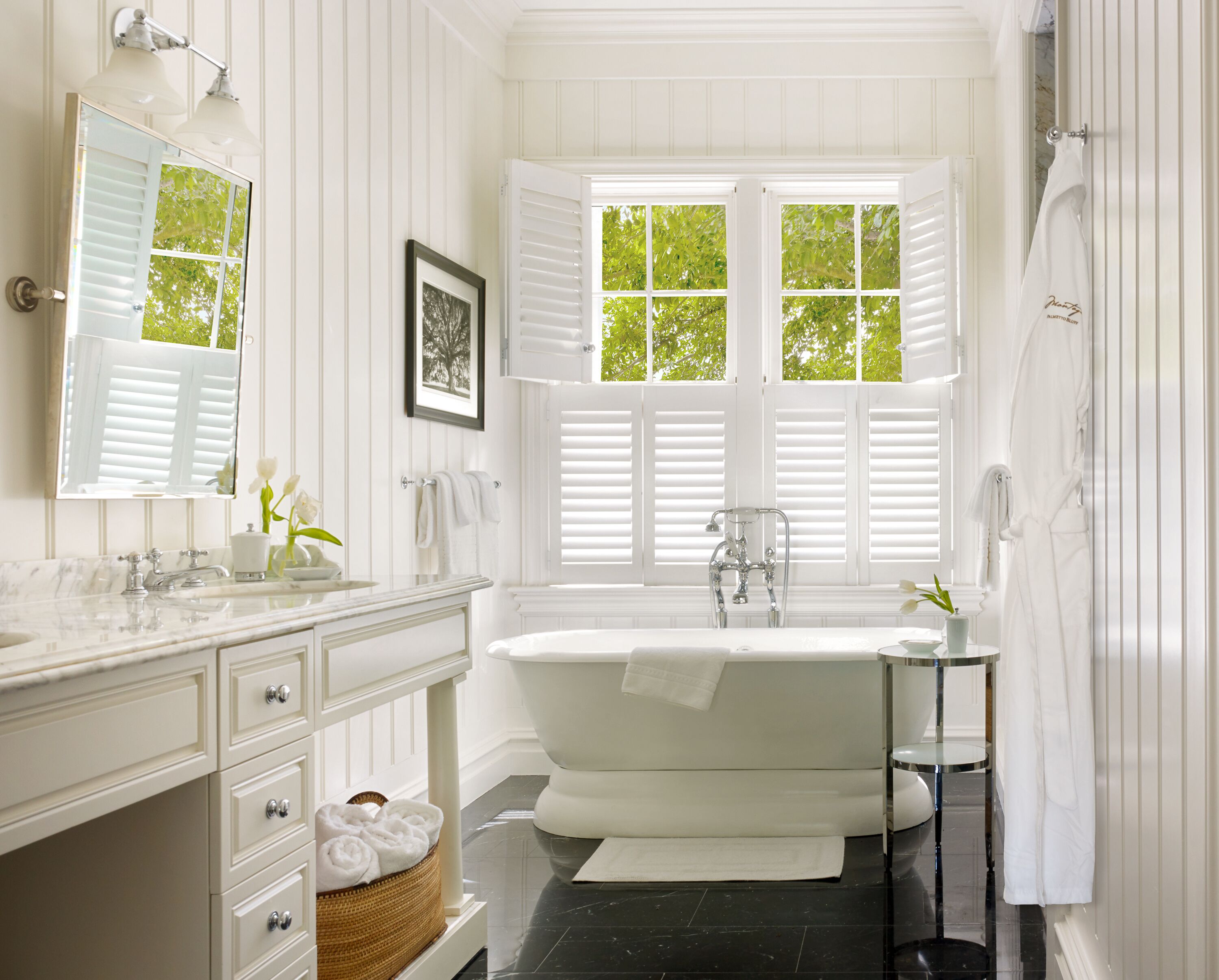 A bathroom with a white vanity, a bathtub, and a window with shutters.