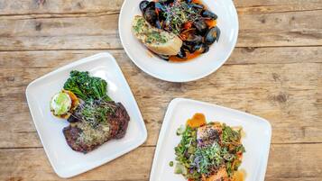 Three square white plates of food on a wooden table.