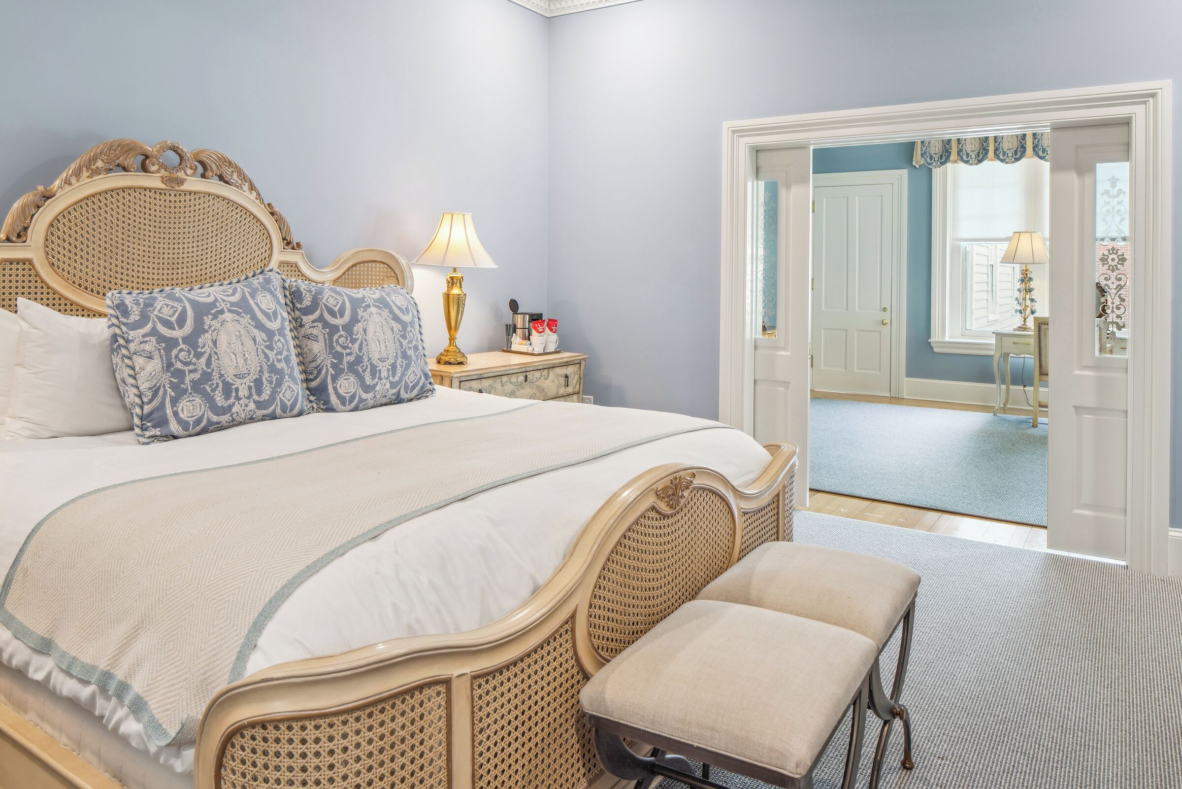 Un dormitorio con una cama grande, una mesita de noche con lámpara y una puerta que da a otra habitación.