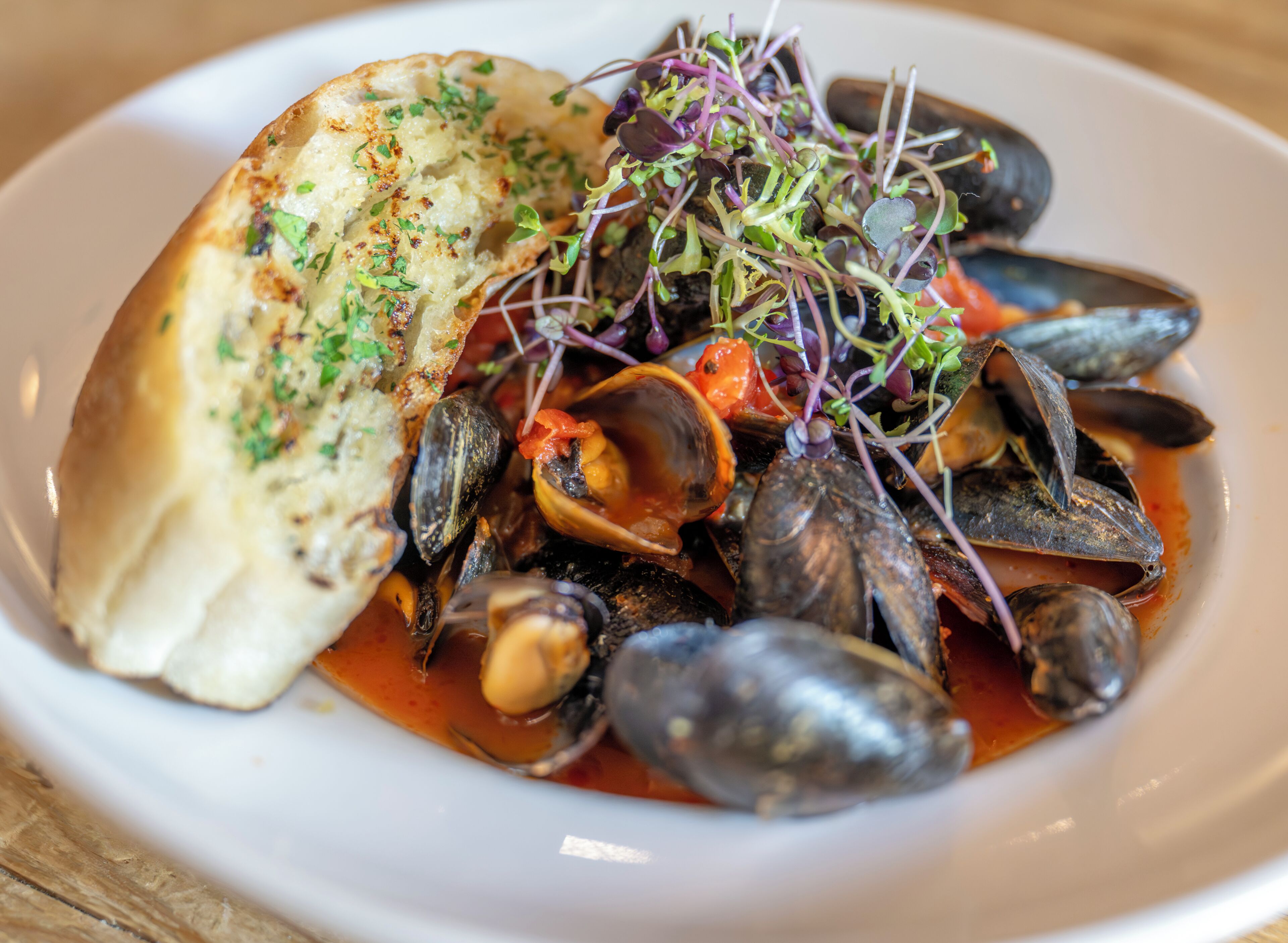 A seafood dish with mussels and a piece of bread on a plate.