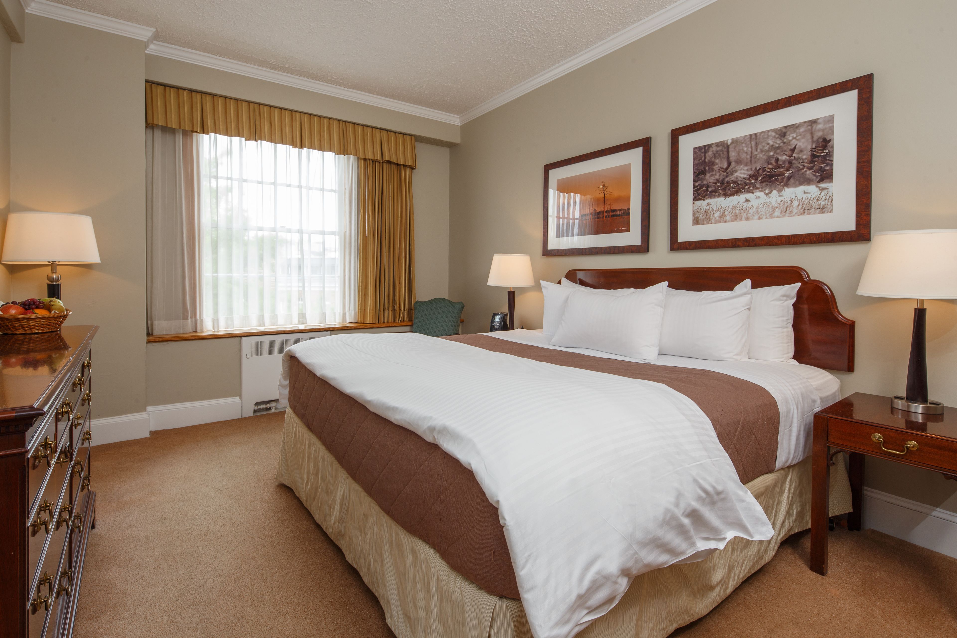 A hotel room with a large bed, two bedside tables, a dresser, and a window with curtains.