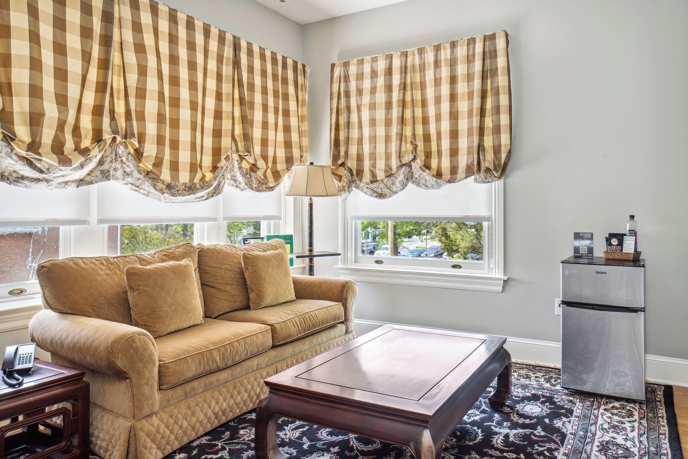 A living room with a beige sofa, a wooden coffee table, a patterned rug, and a refrigerator.