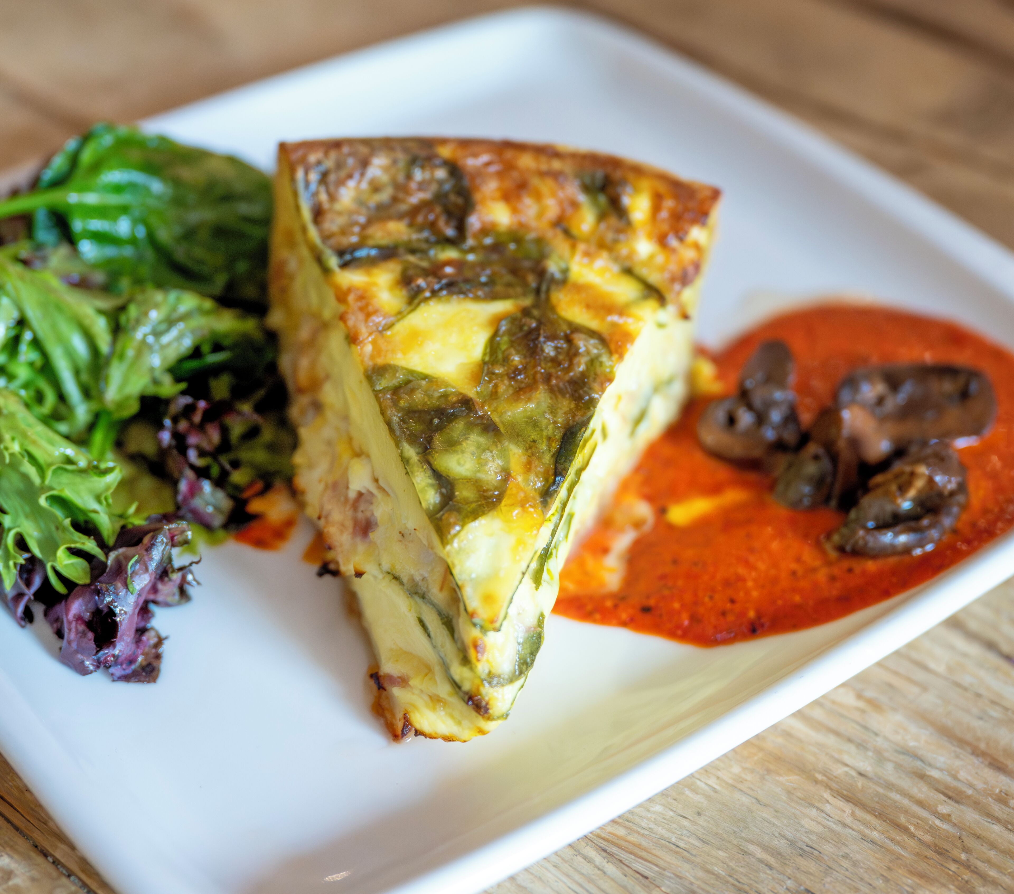 Una fetta di quiche con un’insalata e salsa rossa ai funghi.