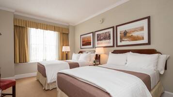Una habitación de hotel con dos camas, un ventanal con cortinas y tres cuadros en la pared.