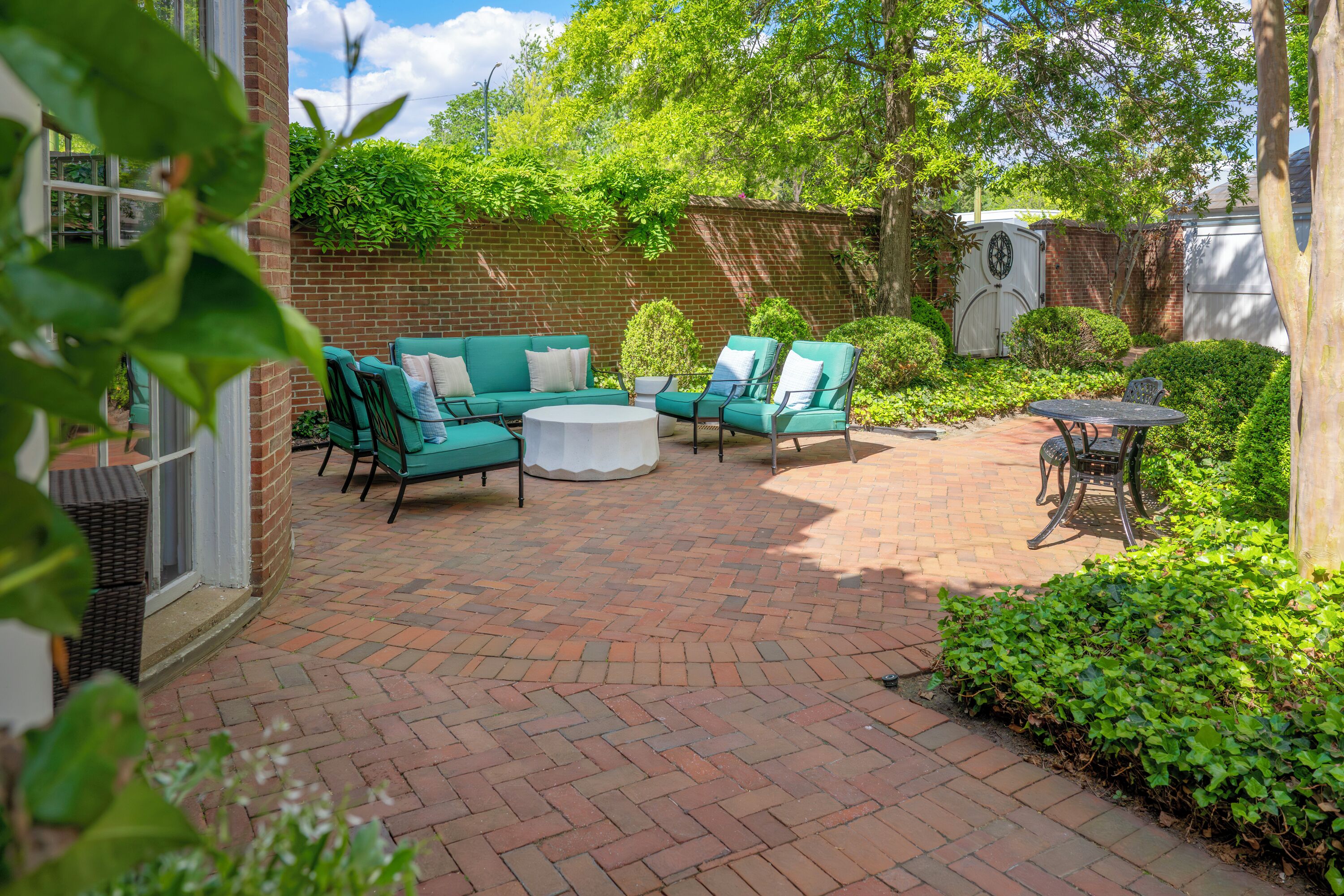 A patio with green furniture, a brick floor, and a brick wall.
