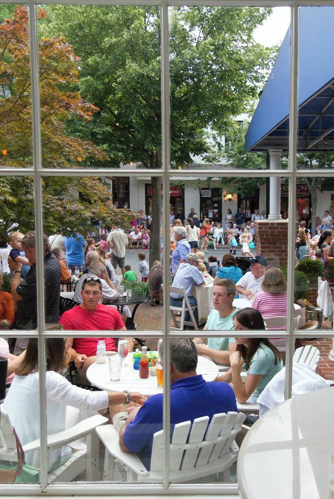 An outdoor seating area with tables and chairs, surrounded by trees and a brick wall.