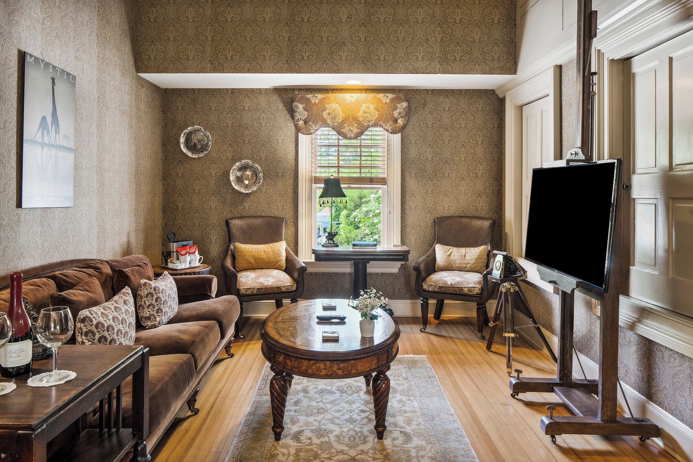 Una sala de estar con un sofá marrón, dos sillones, una mesa de centro y un televisor sobre un mueble.
