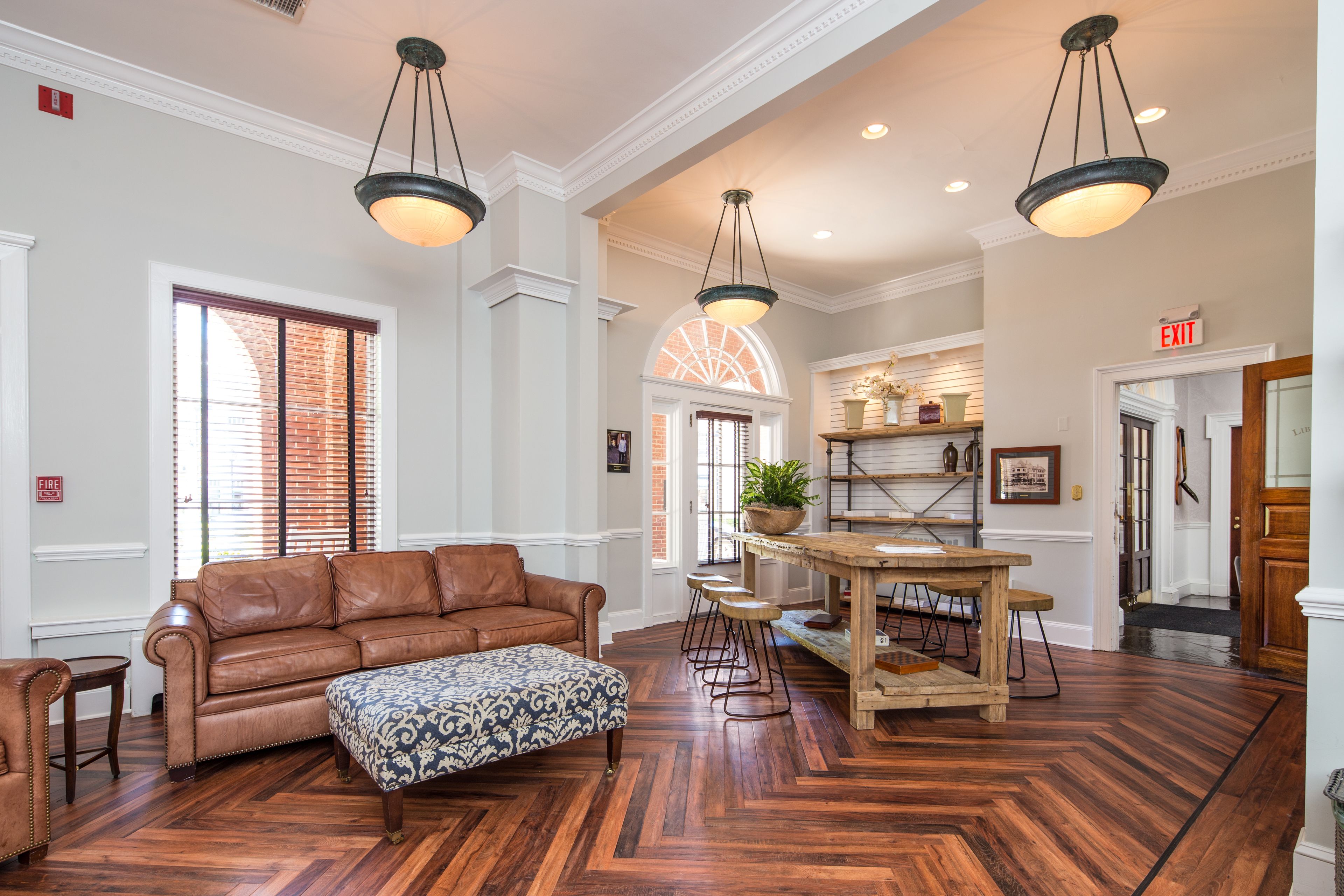 A spacious lobby with a brown leather sofa, patterned ottoman, and a wooden dining table with bar stools.